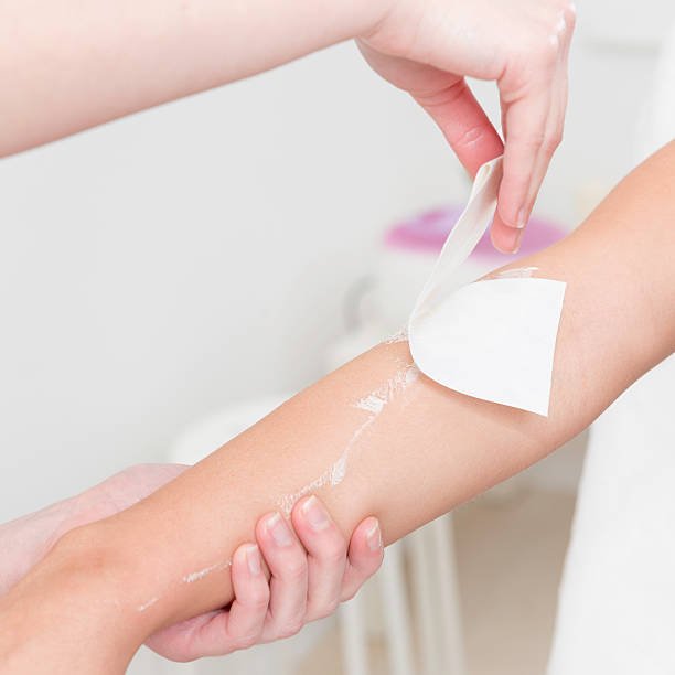 Beautician waxing woman's arm in beauty salon